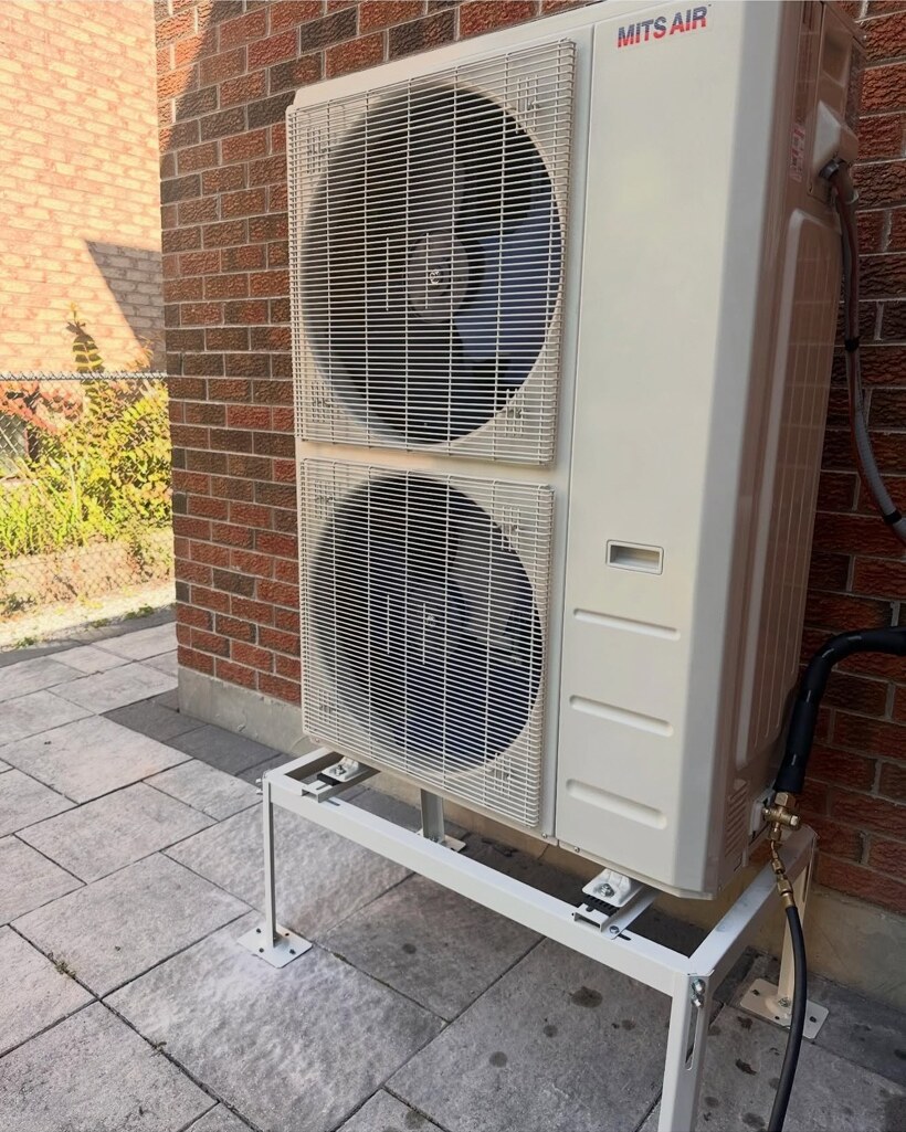 Mits Air cold-climate heat-pump outdoor unit professionally installed on a raised equipment stand beside a brick home